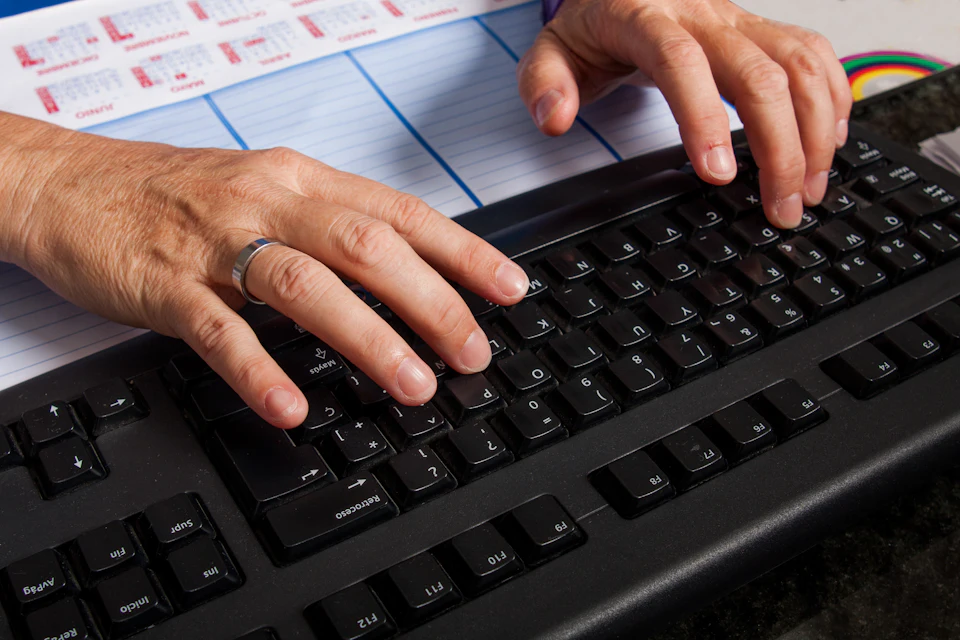 Mains sur un clavier d'ordinateur, avec un planning papier en arrière-plan
