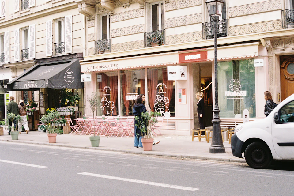 Rue commerçante parisienne avec boutiques, terrasses et une camionnette blanche garée