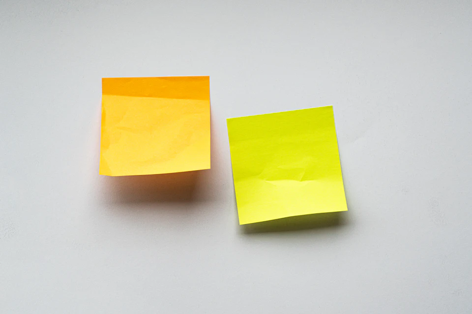 Deux notes adhésives, jaune et vert, collées sur un mur blanc